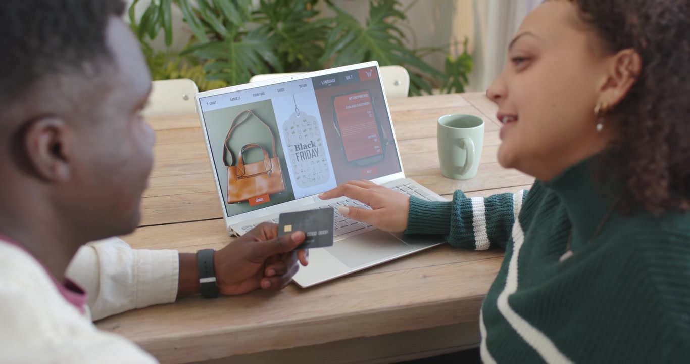 African American couple holding card browsing laptop at table checking Black Friday deciding to buy