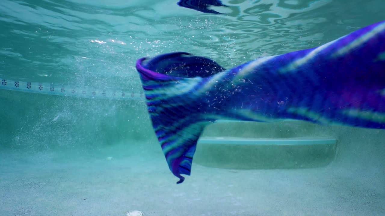 una mujer de pelo rubio nada bajo el agua con cola de sirena mientras viaja de vacaciones.