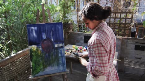 Biracial-female-artist-taking-picture-of-her-painting-using-smartphone-in-sunny-garden,-slow-motion