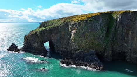 drone reveal from sea cave and cliffs to view of coastline emerald sea and mountain with dramatic clouds in background in waterford ireland