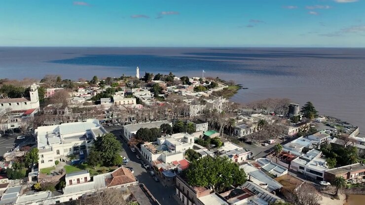 Sorvolo aereo in avanti di Colonia del Sacramento sul paesaggio urbano storico del lungomare e sul faro vicino al fiume