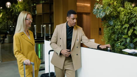 una mujer rubia y un hombre afroamericano hablando en un hotel.