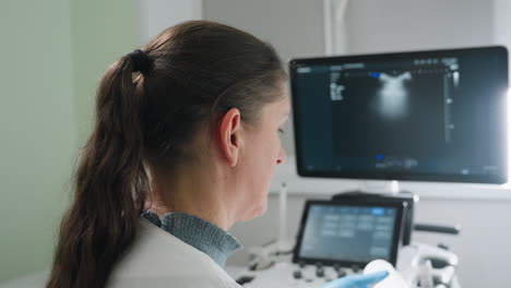 medical laboratory scientist applies gel on transducer while maintaining strong focus on monitor displaying internal scan results in clinical environment, showing precision during diagnostic process