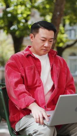 asian man freelancer sitting on city street opens laptop start working online distant job outdoors