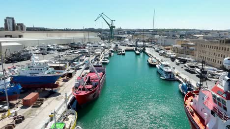 aerial drone shot flying backwards, low and over blue sea in between several boats and ships in a very busy boat yard