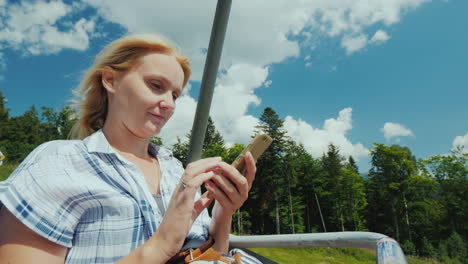 a woman uses a smartphone rides in the open cabin of the cable car on vacation in connection with th