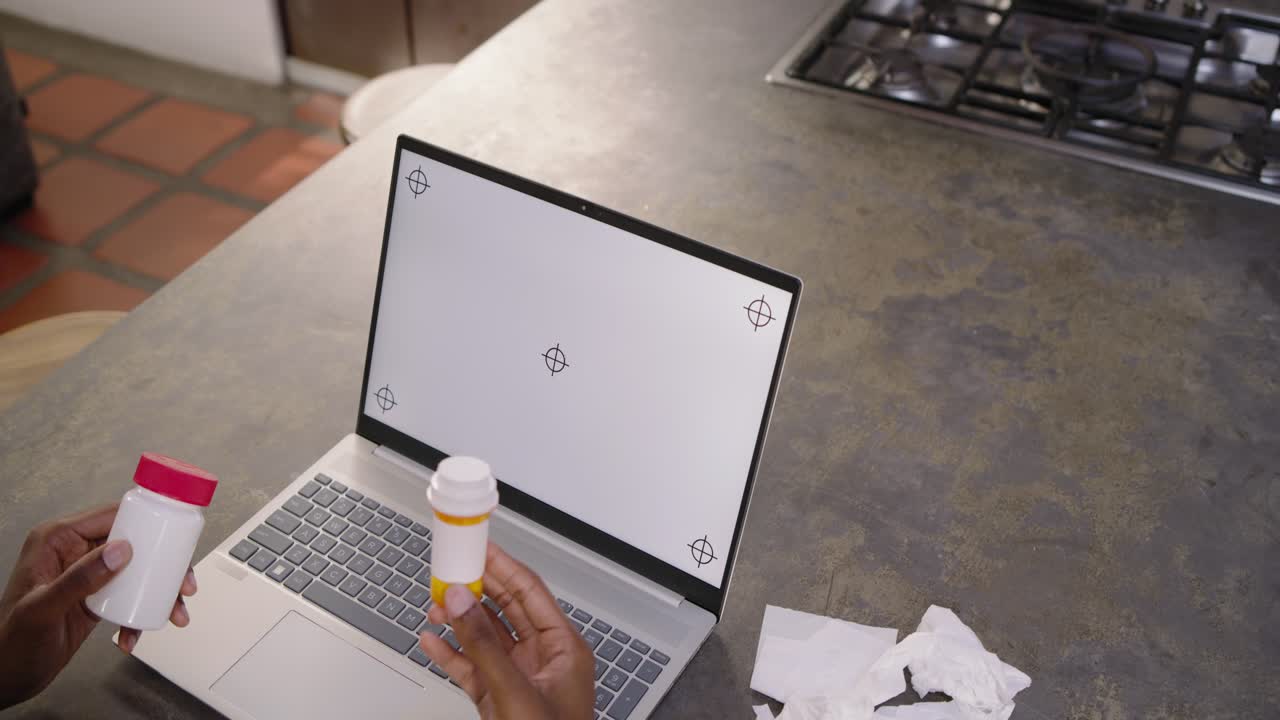 Guardando lo schermo del laptop, un uomo afroamericano controlla le etichette dei farmaci sul bancone della cucina, con spazio per il testo.