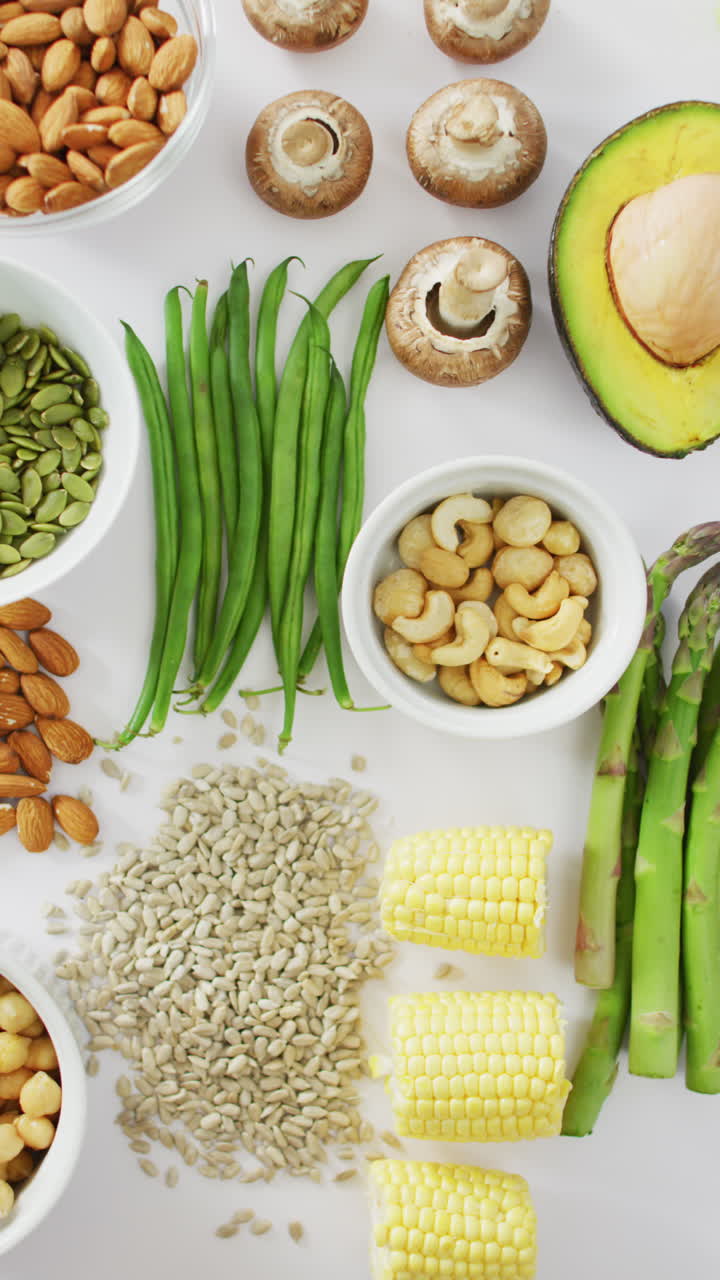 video vertical de alto ángulo de aguacate fresco, frijoles, setas, maíz y espárragos en blanco