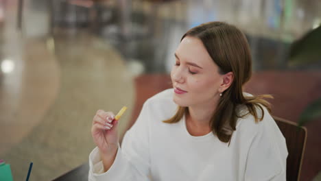 close-up of lady enjoying fries with a warm smile in a mall setting, casual dining moment reflecting satisfaction and joy, with soft blurred background