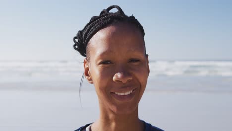 donna afroamericana che guarda la telecamera e sorride sulla spiaggia e sullo sfondo del cielo blu