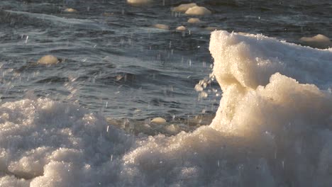 slow motion, close up shot of waves breaking over icy shore in golden light