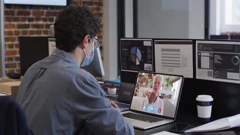 caucasian man on laptop video chat wearing face mask in office