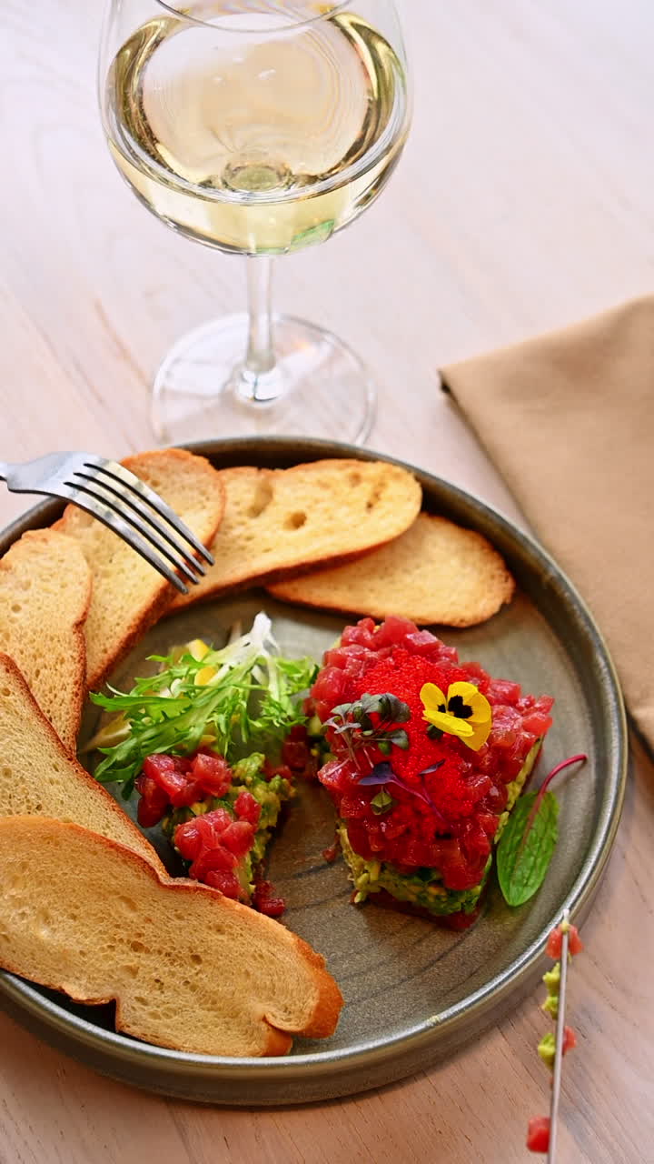 Vino bianco con tartare di tonno. Bicchiere di vino bianco accanto a tartare di tonno e strati di avocado