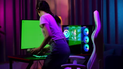 asian teen girl gamer sitting and play video game on computer with mock up green screen