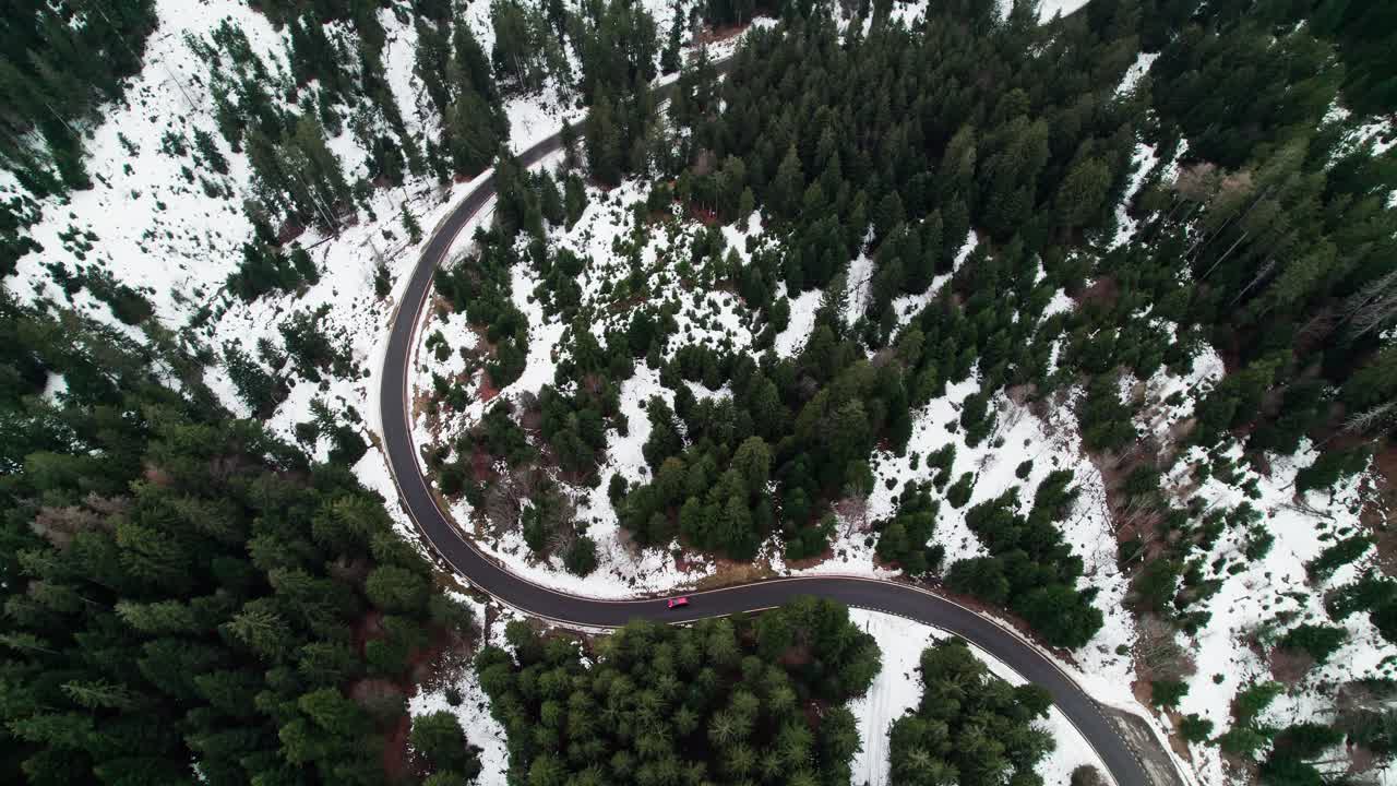 Red car drives on windy road on a mountain pass in Switzerland, snow on ground