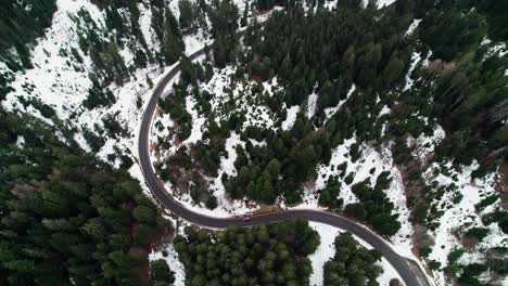 Coche-Rojo-Conduce-Por-Una-Carretera-Ventosa-En-Un-Paso-De-Montaña-En-Suiza,-Nieve-En-El-Suelo