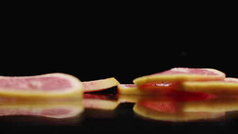 cámara lenta. anillos de pomelo en rodajas que caen con salpicaduras de agua en el vidrio sobre un fondo oscuro. cortado en rodazas