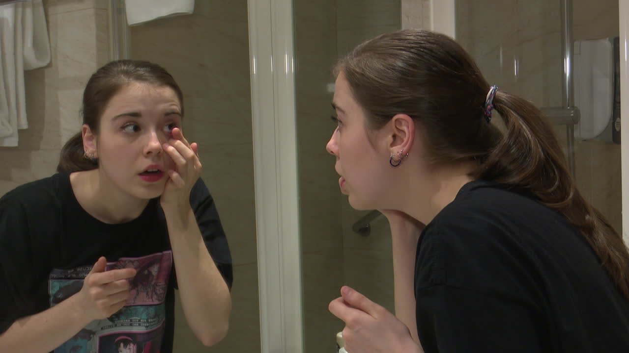 Young woman applying cream in front of a bathroom mirror