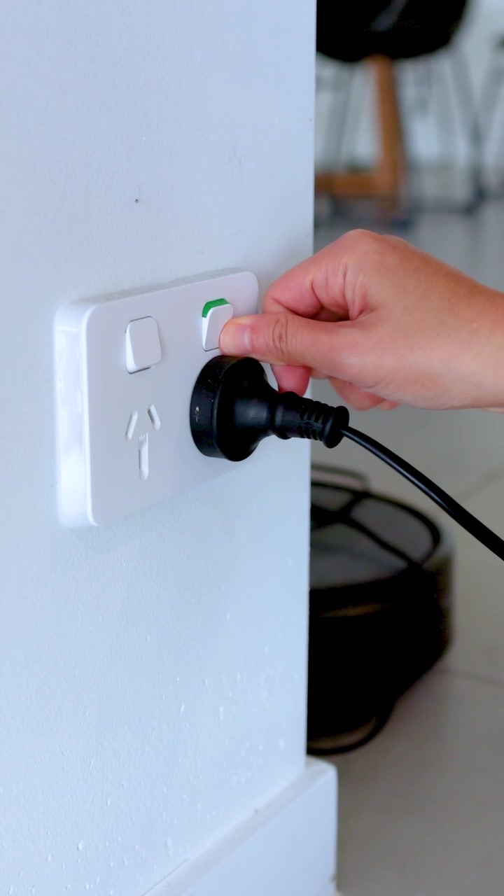 A hand plugs a power cord into a wall socket in a well-lit room, highlighting everyday electrical use
