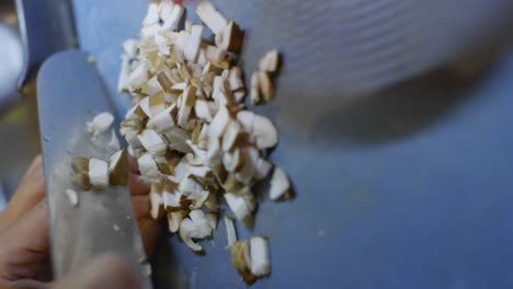 hongo cortado en pedazos pequeños usando un cuchillo de cocina en una tabla de cortar azul, filmado como un primer plano vertical en cámara lenta de mano