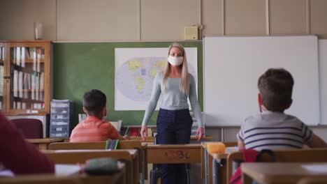 una maestra con una mascarilla hablando con los niños en el aula de la escuela.