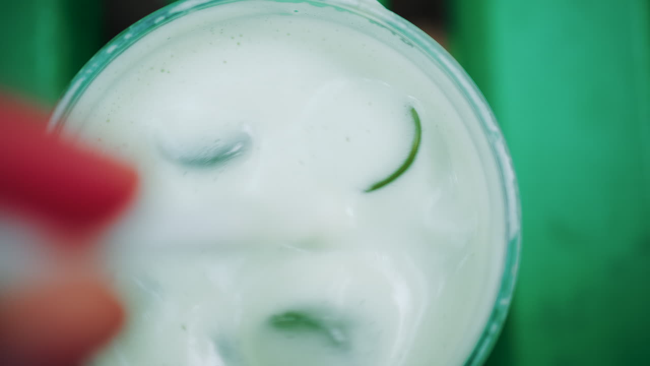 Close up of a white liquid being stirred in a glass with ice