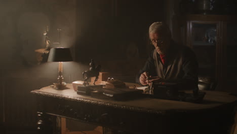older passionate man evaluates an old silver skull watch in his office at night