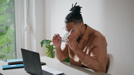 Focused-man-taking-glasses-on-in-office-closeup.-Dreadlocks-guy-working-laptop