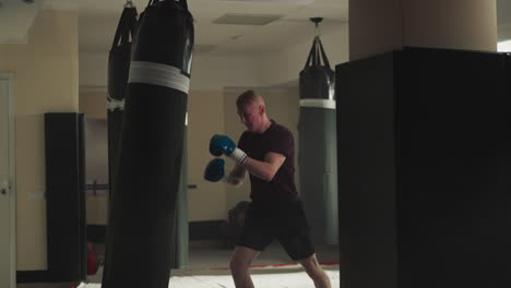 el hombre fuerte patea la bolsa de boxeo con las rodillas en el gimnasio. el kickboxer hábil hace ejercicios con equipos en el club deportivo en cámara lenta. el hombre fuerte entrena en combate.