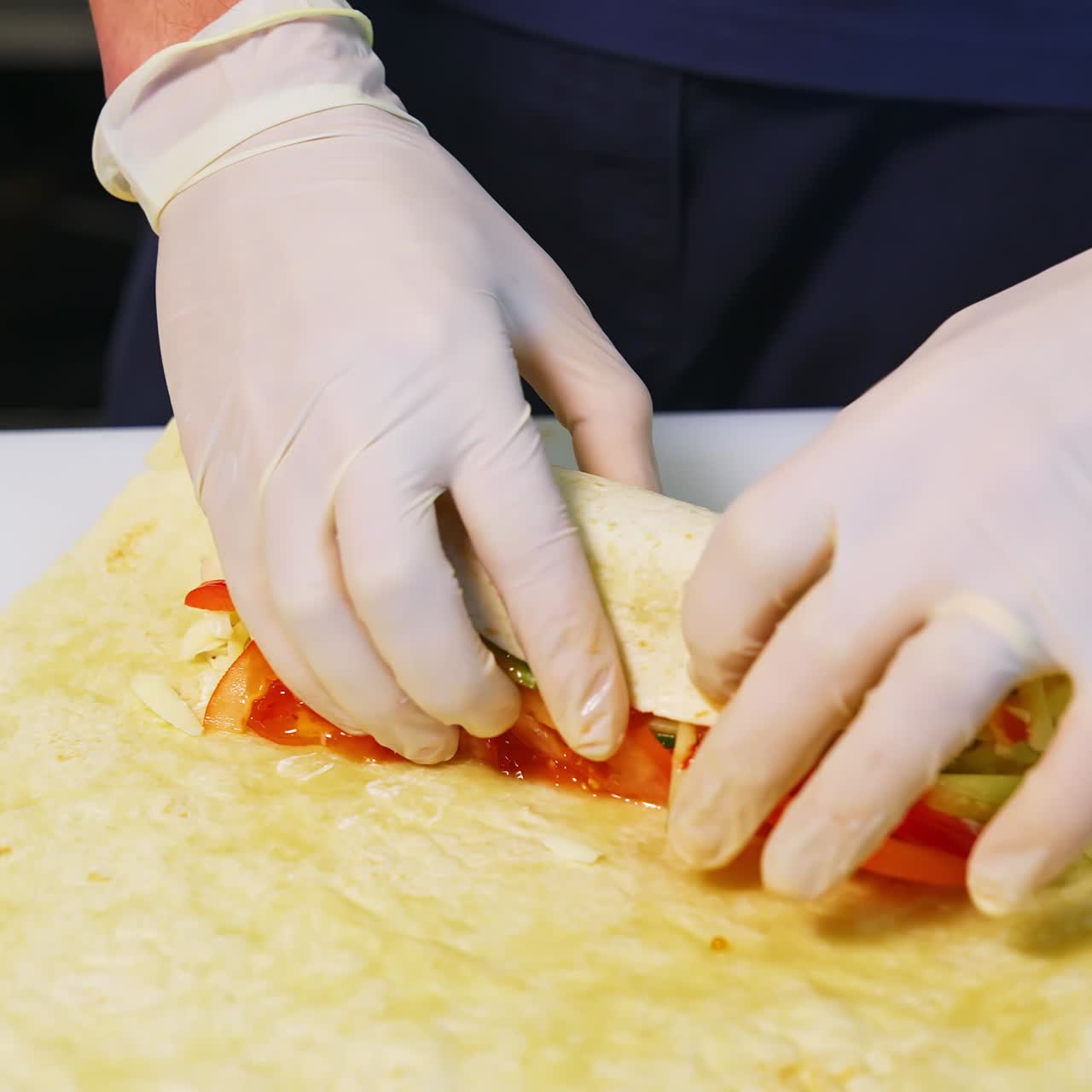 Cooking meat and cheese pita with vegetables. Hands in latex gloves roll up a pita roll. Concept video