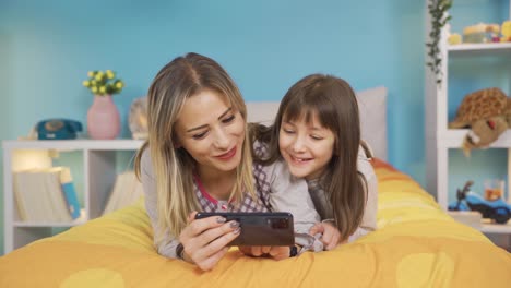 Mamá-Y-Su-Pequeña-Hija-Están-Jugando-Con-El-Teléfono-En-La-Cama-En-Casa.