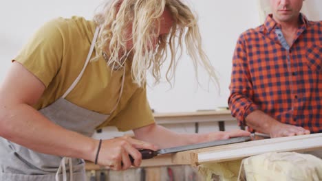 Two-Caucasian-male-surfboard-makers-working-in-their-studio-and-making-a-wooden-surfboard-together