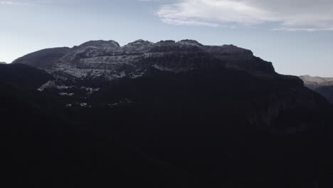 this drone video showcases a stunning frontal descriptive shot over the hecho valley in the aragonese pyrenees, spain, with snowy mountains in the background under a cloudy sunset sky.