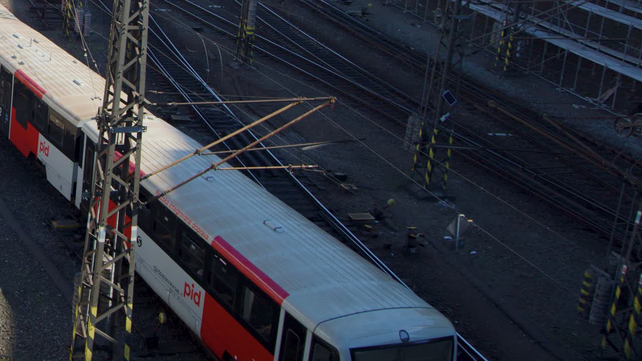 A red and white passenger train leaves the main railway station in Prague, captured from above in soft evening light with minimal camera movement