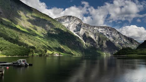 heavy clouds move fast above the calm norwegian naeroy fjord and forest-covered mountains, casting dark shadows