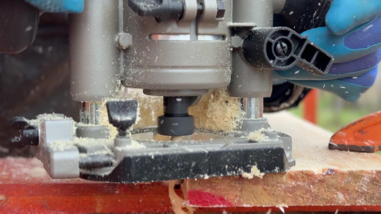 Artisan défonçant le bord d'une longue planche en bois avec une défonceuse portative sur un établi extérieur, façonnant la surface du bois tout en produisant de fins copeaux