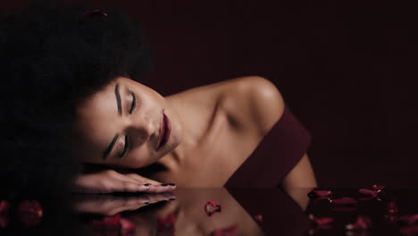 Retrato-Hermosa-Mujer-Afroamericana-Relajante-Pétalos-De-Rosa-Cayendo-Sobre-La-Piel-Suave-Mujer-Sensual-Soñando-Con-Un-Romance-De-Fantasía-íntima-Que-Complace-El-Deseo-En-El-Concepto-Del-Día-De-San-Valentín-Rojo