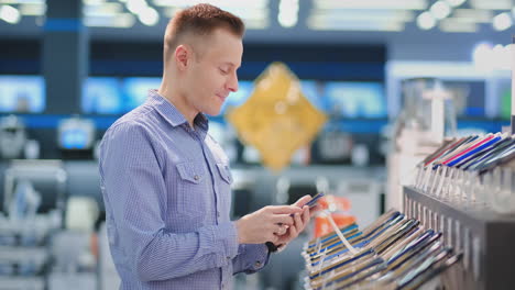 a man standing at a shop window with smartphones chooses a new phone model to buy a portable electronics store. purchase the latest version of the gadget