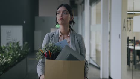 final de la carrera. joven despedida mujer molesta caminando por el edificio de oficinas, llevando caja con pertenencias personales y llorando
