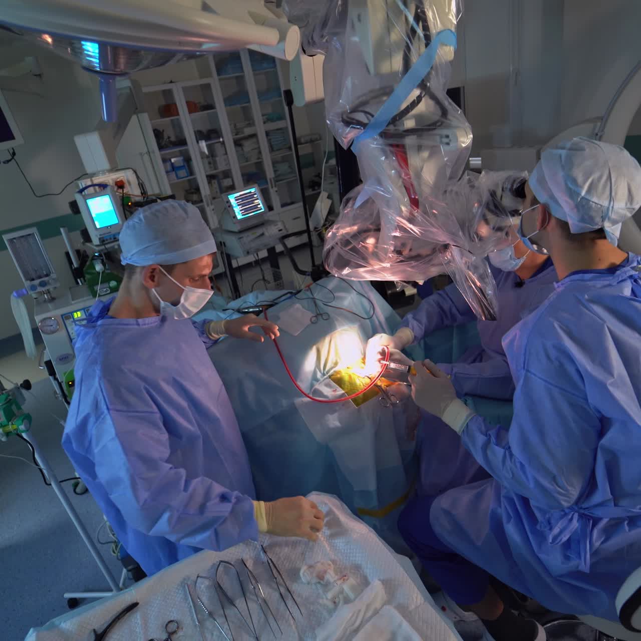 Performing operation in surgery room. Neurosurgeon holds a syringe and looks in binoculars. Assistants adjust tubes to the place of intervention
