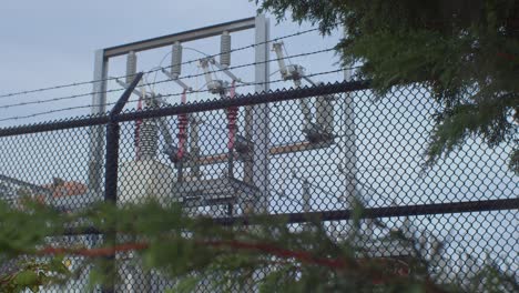 Electrical-power-plant-sub-station-protected-by-barbed-wire-fence---behind-trees---medium-shot