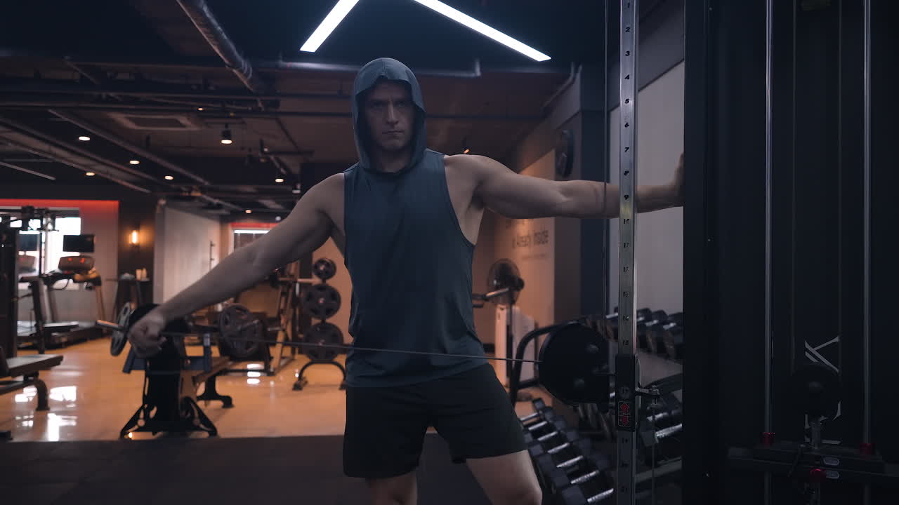 Sporty Man Trains Shoulders in Gym, Wearing Tank Top With Hood