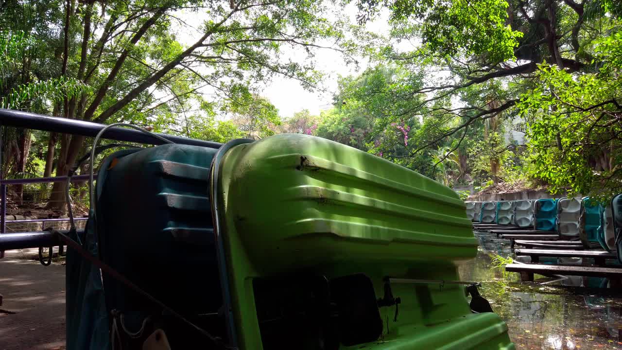 Colorful pedal boats resting near the canal, surrounded by lush trees and dappled light