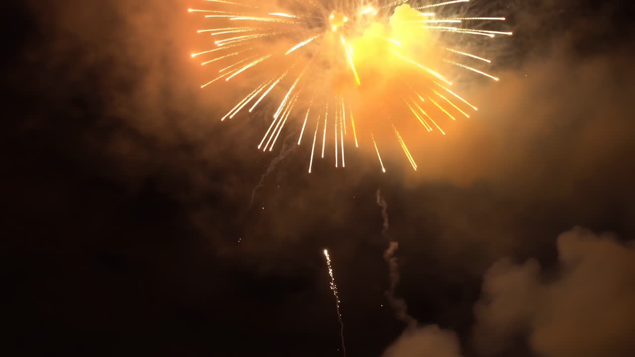 Fuochi d'artificio dorati esplodono nel cielo notturno, grandi proiettili aerei si trasformano in scie dorate e bianche scintillanti, spesse.