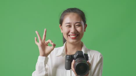 close up of asian photographer looking at the pictures in the camera and showing okay gesture while standing on green screen background in the studio