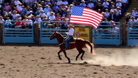 man on horseback carrying american flag at a rodeo event