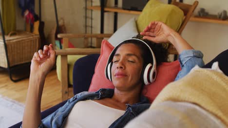 mujer caucásica escuchando música con auriculares, acostada en el sofá en casa