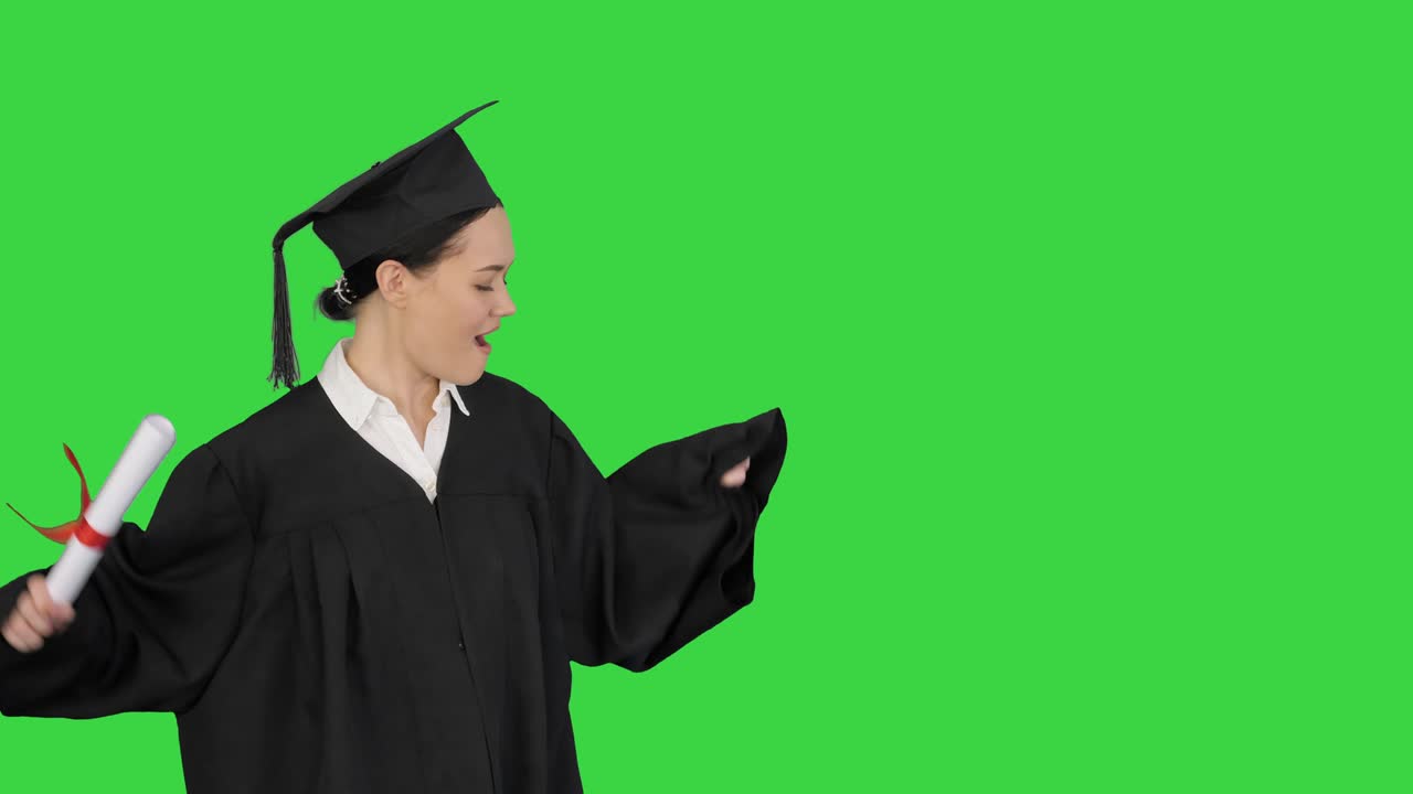 Studentessa felice in toga di laurea che cammina ed esulta con il suo diploma su schermo verde, Chroma Key.