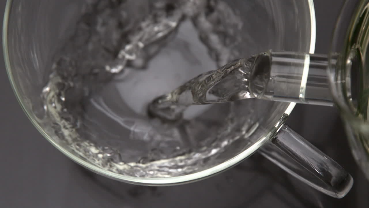 Acqua calda che si versa dalla teiera in una tazza di vetro