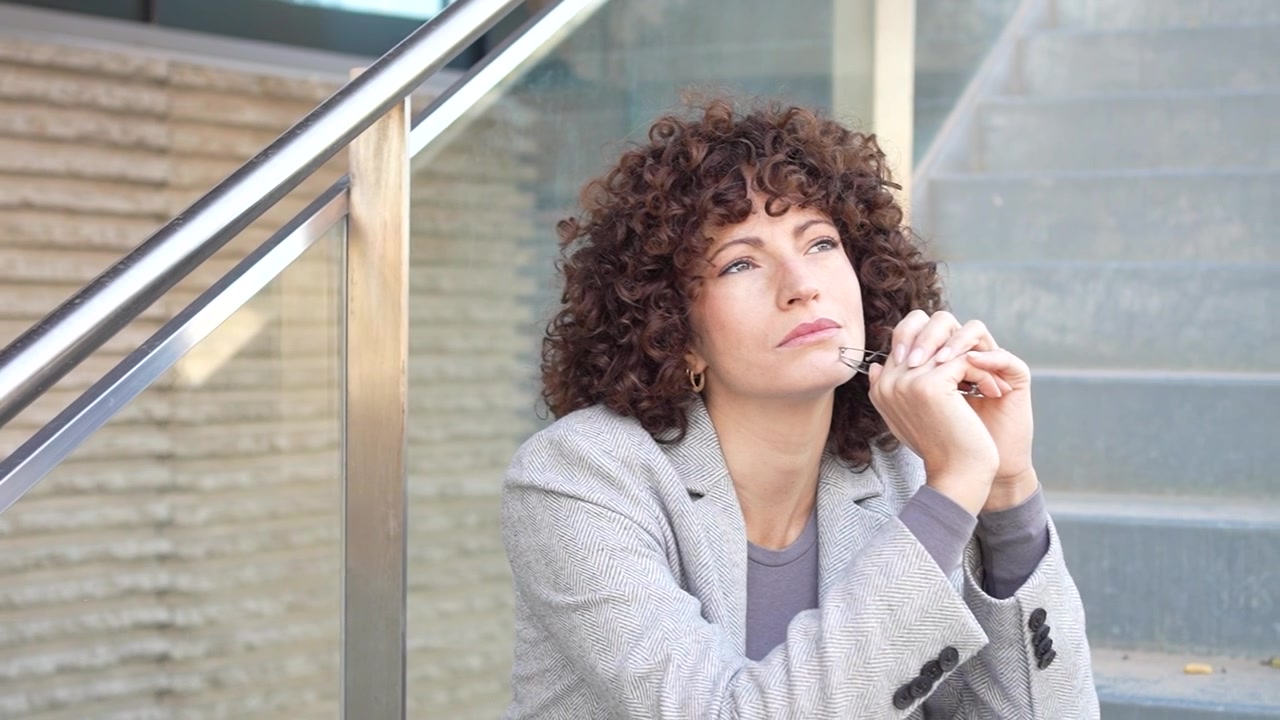 Una donna pensierosa con bellissimi capelli ricci è seduta sulle scale in modo contemplativo.
